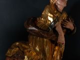 statue of a man in a golden robe sitting on a black surface