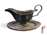a silver gravy with a saucer on a plate