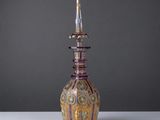 un vase violet et doré, surmonté d'un couvercle doré, posé sur une table blanche