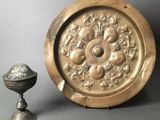 a gold plate with a flower design on it next to a silver cup