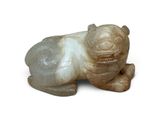 une petite figurine représentant un chien couché sur une surface blanche