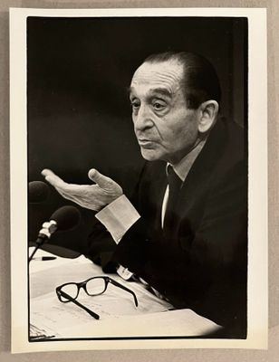photographie en noir et blanc d'un homme assis à une table, avec un micro devant lui
