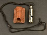 a small metal whistle and a leather case on a table