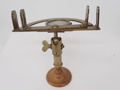 un télescope ancien plaqué laiton, posé sur un socle en bois, sur une surface blanche