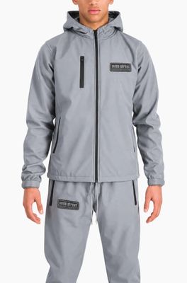 un homme vêtu d'une veste et d'un pantalon gris, debout devant un fond blanc