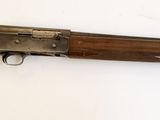Un vieux fusil est posé sur une surface blanche, devant un fond blanc.