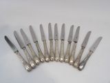 six silverplated knives are lined up on a white surface