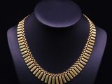 a gold necklace on a mannequin with a black background