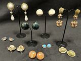 several pairs of earrings and brooches are displayed on a stand