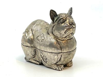 une figurine en argent représentant un chat assis sur une surface blanche