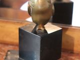 a gold bird statue on a black stand in front of a mirror