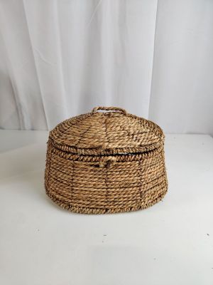 un petit panier tressé muni d'un couvercle, posé sur une surface blanche