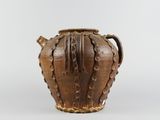 an old brown vase sitting on top of a table next to a white wall