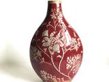 un vase rouge orné de fleurs blanches, posé sur un fond blanc
