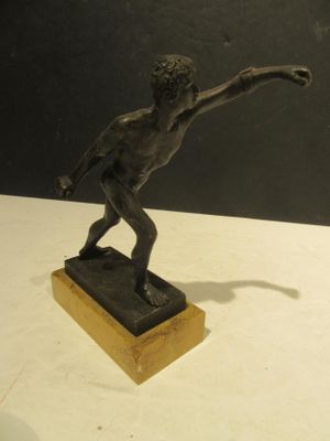 statue en bronze représentant un garçon lançant un frisbee, posée sur un socle en bois