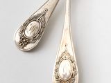 pair of silver spoons on a white surface with a picture of a woman on the spoon