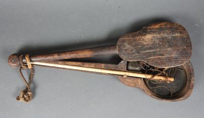 un vieil instrument en bois muni d'un manche en bois, posé sur une surface grise