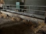 a metal trough with hay on the ground in a barn