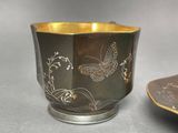 a silver cup with a butterfly design on it next to a plate with a plate on it