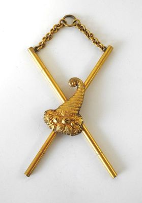une image représentant une broche plaquée or ornée de deux bâtons croisés et d'une boule