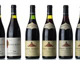 six bottles of wine are lined up on a white surface
