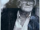 a black and white photo of a man with glasses looking out of a window