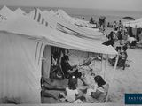 photo en noir et blanc d'un groupe de personnes assises dans des tentes sur une plage