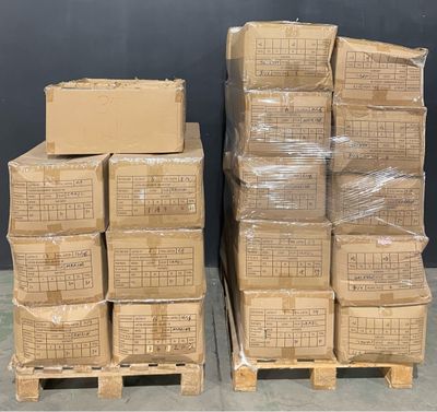 des cartons empilés sur des palettes dans un entrepôt, avec un tableau noir en arrière-plan