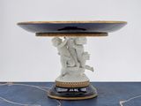 a white and gold plate with a statue on top of it