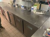 un homme debout dans une cuisine, à côté d'un plan de travail en inox