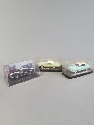 three miniature cars in plastic cases on a white surface