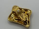 an image of a gold plated pin with a hand holding a gun