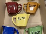 six tasses de couleurs différentes dans une boîte, sur lesquelles figurent des prénoms