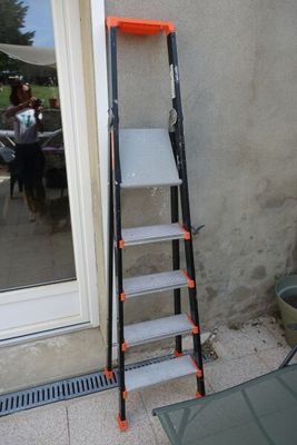 une échelle appuyée contre un mur, à côté d'une table de terrasse