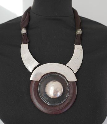 collier en métal et en bois, orné d'un pendentif circulaire, posé sur le cou d'un mannequin