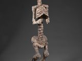 une statue représentant un squelette humain posé sur un rocher, coiffé d'un chapeau