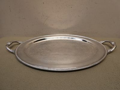 un plateau ovale en argent muni d'anses, sur un fond beige
