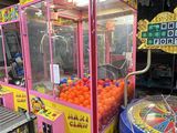 oranges in a pink cart next to an arcade machine