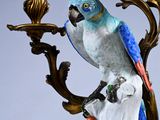 a figurine of a parrot sitting on a branch with a candelab