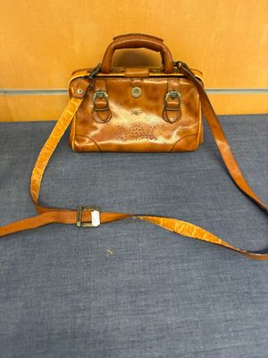 un sac à main en cuir posé par terre, avec une sangle autour