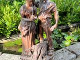 une statue représentant un homme et une femme accompagnés d'un chien dans un jardin