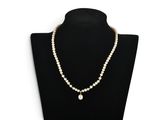 a white pearl necklace with a gold clasp on a black mannequin