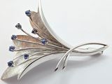 silver brooch with blue stones on it on a white surface