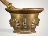 brass mortar with a wooden pestula in it on a white background