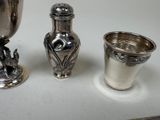 a silver vase, a silver cup, and a silver spoon on a table