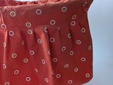 a red bag with a pattern on it and a pair of knitting needles in it