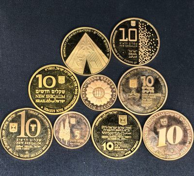 six types différents de pièces israéliennes posées sur un tissu bleu