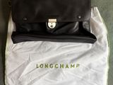 un sac Longchamp noir posé sur un sac blanc, lui-même posé sur un tapis vert