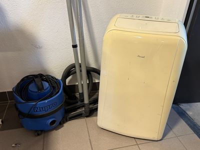 a small white refrigerator next to a vacuum and a blue bucket
