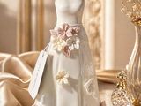 a wedding dress on a table next to a vase of flowers
